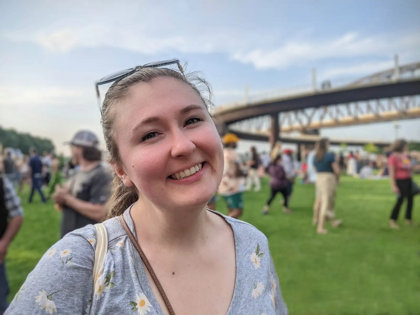 Dr. Anna Reed in a park with many people and a bridge in the background. She is looking at the camera and smiling.